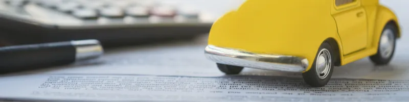 petite voiture jaune près d'un stylo et d'une calculatrice